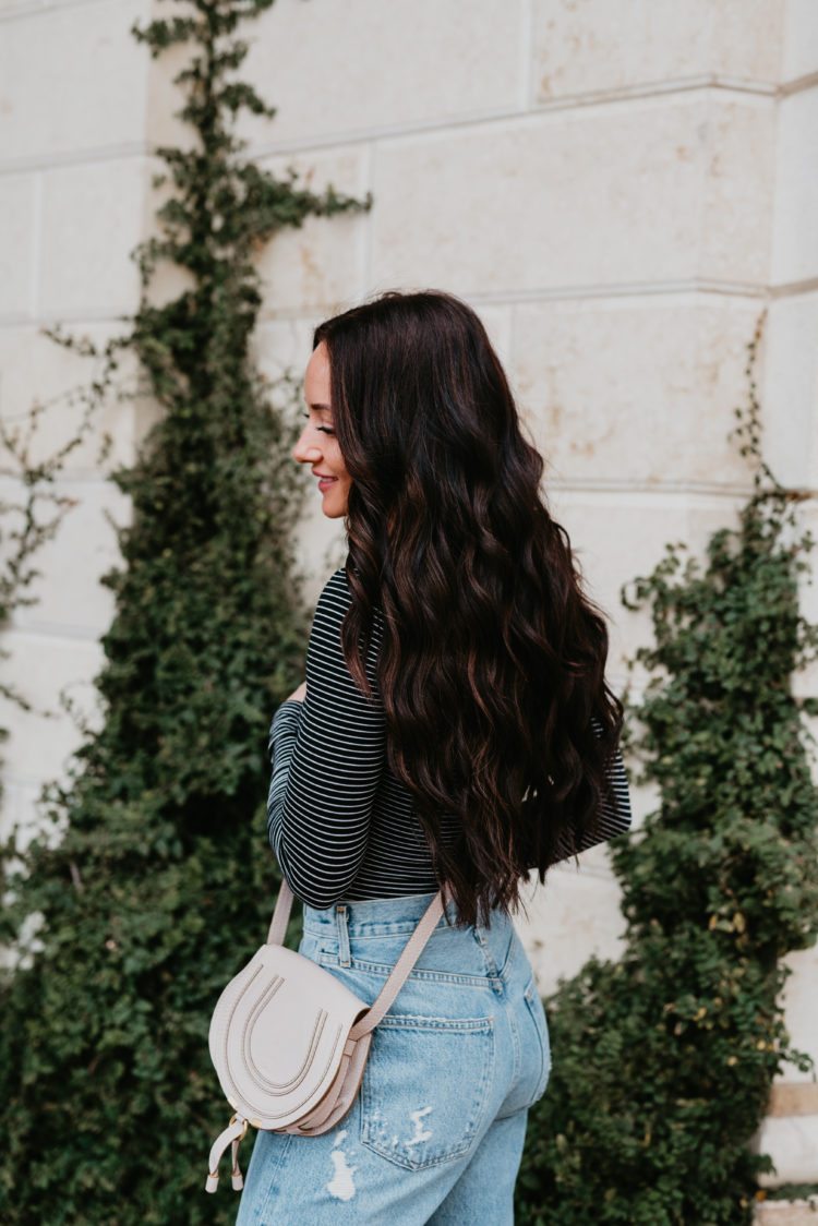Natural Beaded Extensions by popular Las Vegas beauty blog, Outfits and Outings: image of a woman with long brown wavy hair and wearing a black and white stripe top and light wash jeans. 