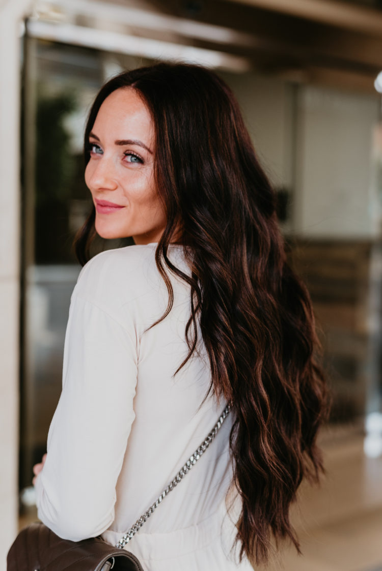 Natural Beaded Extensions by popular Las Vegas beauty blog, Outfits and Outings: image of a woman with long brown wavy hair and wearing a white button up long sleeve top and light wash denim while holding a ysl purse. 