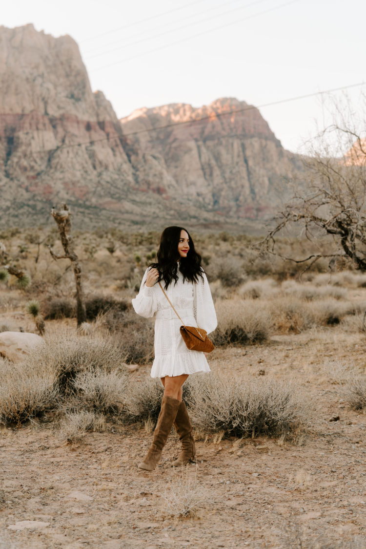 Family Picture Ideas by popular Las Vegas fashion blog, Outfits and Outings: image of a woman standing in the desert and wearing a white eyelet dress and brown suede boots. 