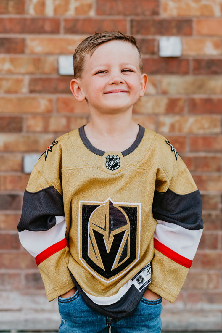 Golden Knights Gear by popular Las Vegas fashion blog, Outfits and Outings: image of a young boy standing in front of a brick wall and wearing a Golden Knights jersey. 