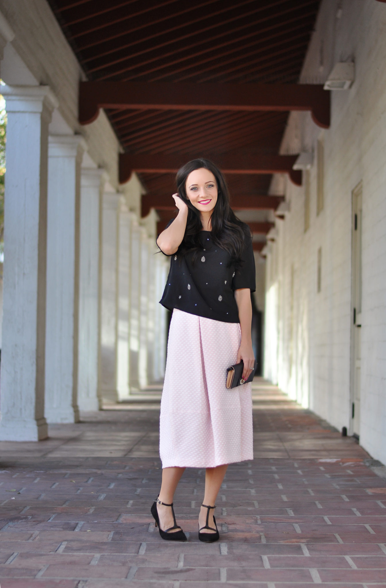 Cute Spring Outfits featured by top US fashion blog Outfits & Outings; Image of a woman wearing black top and pink skirt.