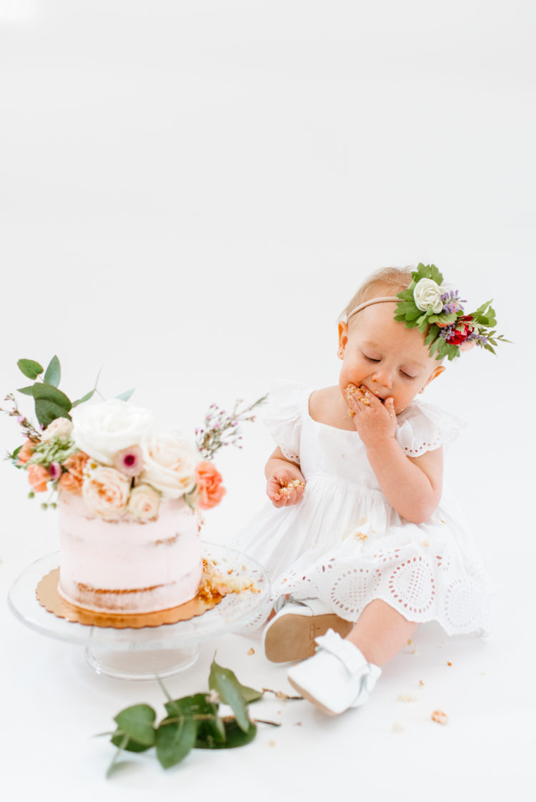 One Year Old Cake Smash Photoshoot featured by top US lifestyle blog, Outfits & Outings: image of a baby girl wearing a GAP eyelet dress and Freshly Picket moccasins with her smash cake