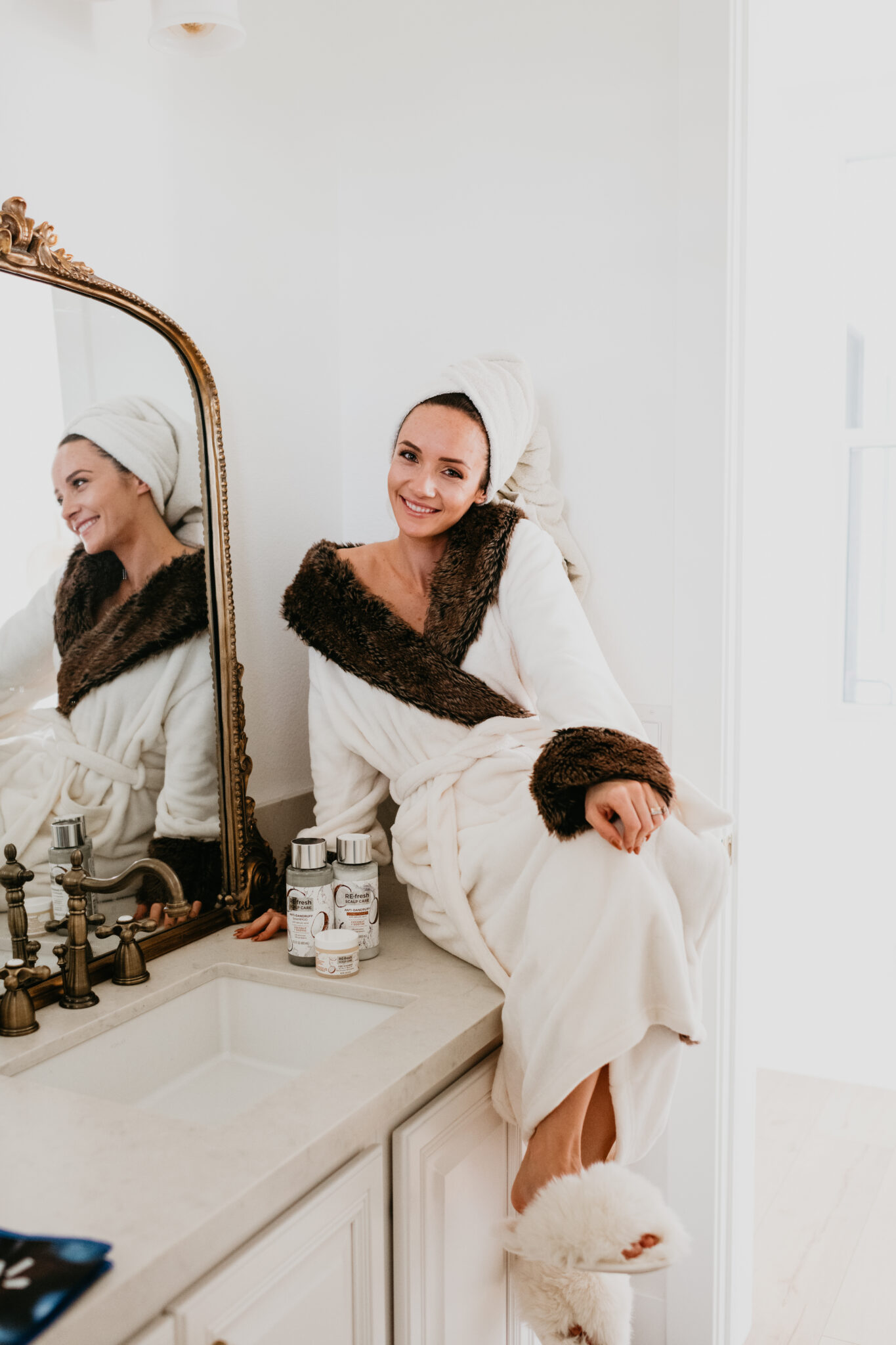 Re-fresh scalp care review: the best products for dandruff. A review featured by top Las Vegas beauty blog, Outfits and Outings | Re-Fresh Scalp Care by popular Las Vegas hair and beauty blog, Outfits and Outings: image of a woman wearing a white bathrobe and sitting on her bathroom counter next to some Re-Fresh Scalp Care products.