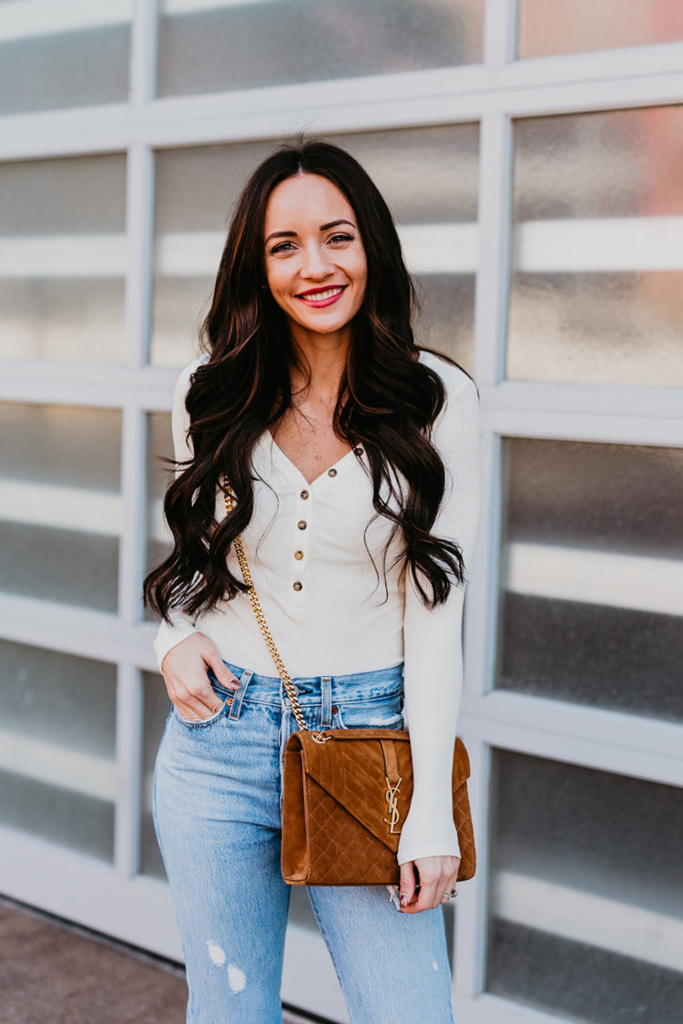 Natural Beaded Extensions by popular Las Vegas beauty blog, Outfits and Outings: image of a woman with long brown wavy hair and wearing a white button up long sleeve top and light wash denim while holding a ysl purse. 
