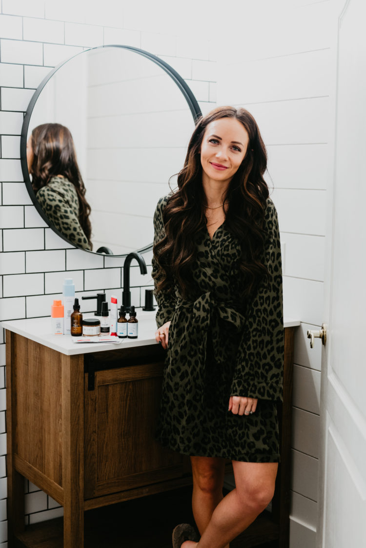 Acne and Anti Aging Skincare Routine by popular Las Vegas beauty blog, Outfits and Outings: image of a woman wearing a green and black leopard print robe and standing next to various acne and skincare products resting on a bathroom counter. 