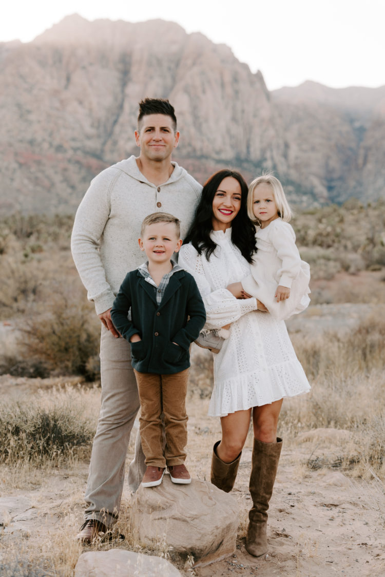 Family Picture Ideas by popular Las Vegas fashion blog, Outfits and Outings: image of a mom, dad, and their young son and young daughter standing in the desert and wearing a white eyelet dress, brown suede boots, grey sweater, tan pants, cream dress, brown pants, brown shoes, and green sweater. 