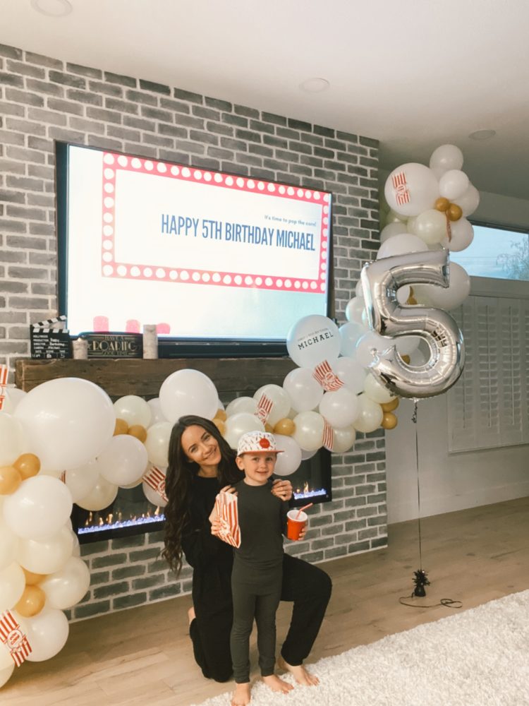 Birthday Party Ideas by popular Las Vegas lifestyle blog, Outfits and Outings: image of a mom and her son wearing matching black pajama sets and standing together in front of popcorn balloon garland. 