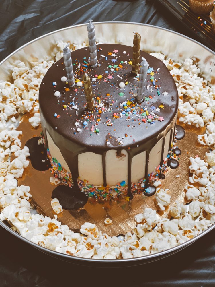 Birthday Party Ideas by popular Las Vegas lifestyle blog, Outfits and Outings: image of a white and chocolate frosting birthday cake topped with rainbow sprinkles and gold and silver candles.
