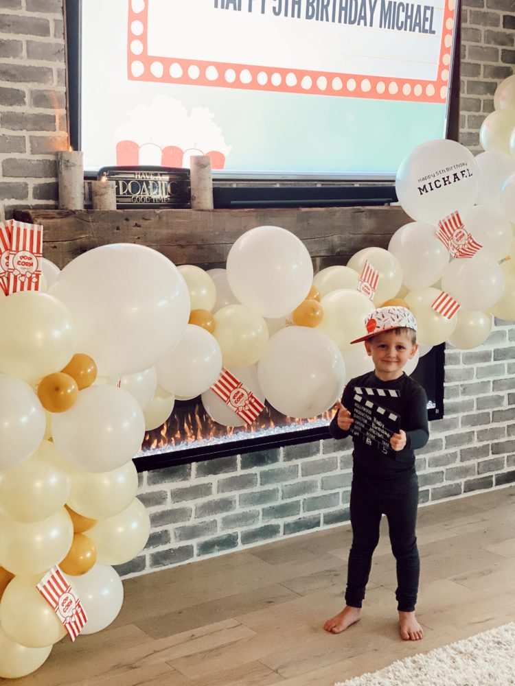 Birthday Party Ideas by popular Las Vegas lifestyle blog, Outfits and Outings: image of a little boy standing in front of a popcorn balloon garland wearing a black pajama set. 