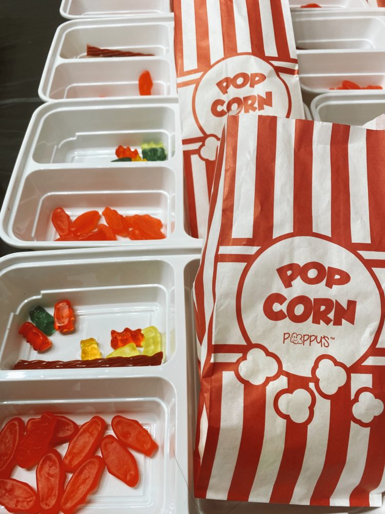 Birthday Party Ideas by popular Las Vegas lifestyle blog, Outfits and Outings: image of white plastic food trays filled with Swedish fish, gummy bears, licorice, and red and white stripe popcorn bags filled with popcorn. 