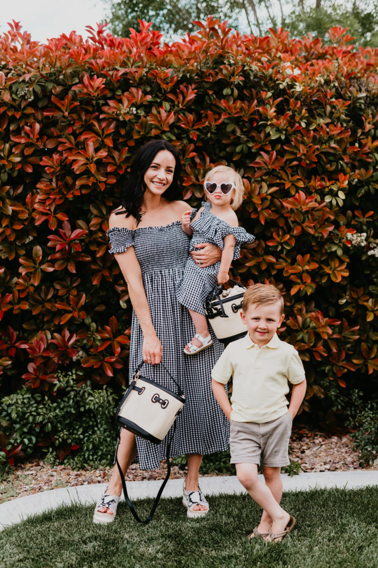 Easter Basket Ideas by popular Las Vegas life and style blog, Outfits and Outings: image of a mom and her two young kids standing together and wearing a black and white gingham off the shoulder midi dress, yellow polo shirt and tan shorts. 