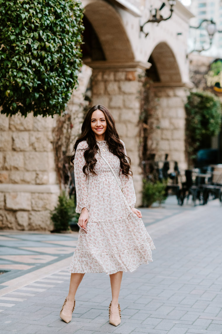 Wedding Guest Dresses by popular Las Vegas fashion blog, Outfits and Outings: image of a woman standing outside and wearing a white floral print dress with high heels. 