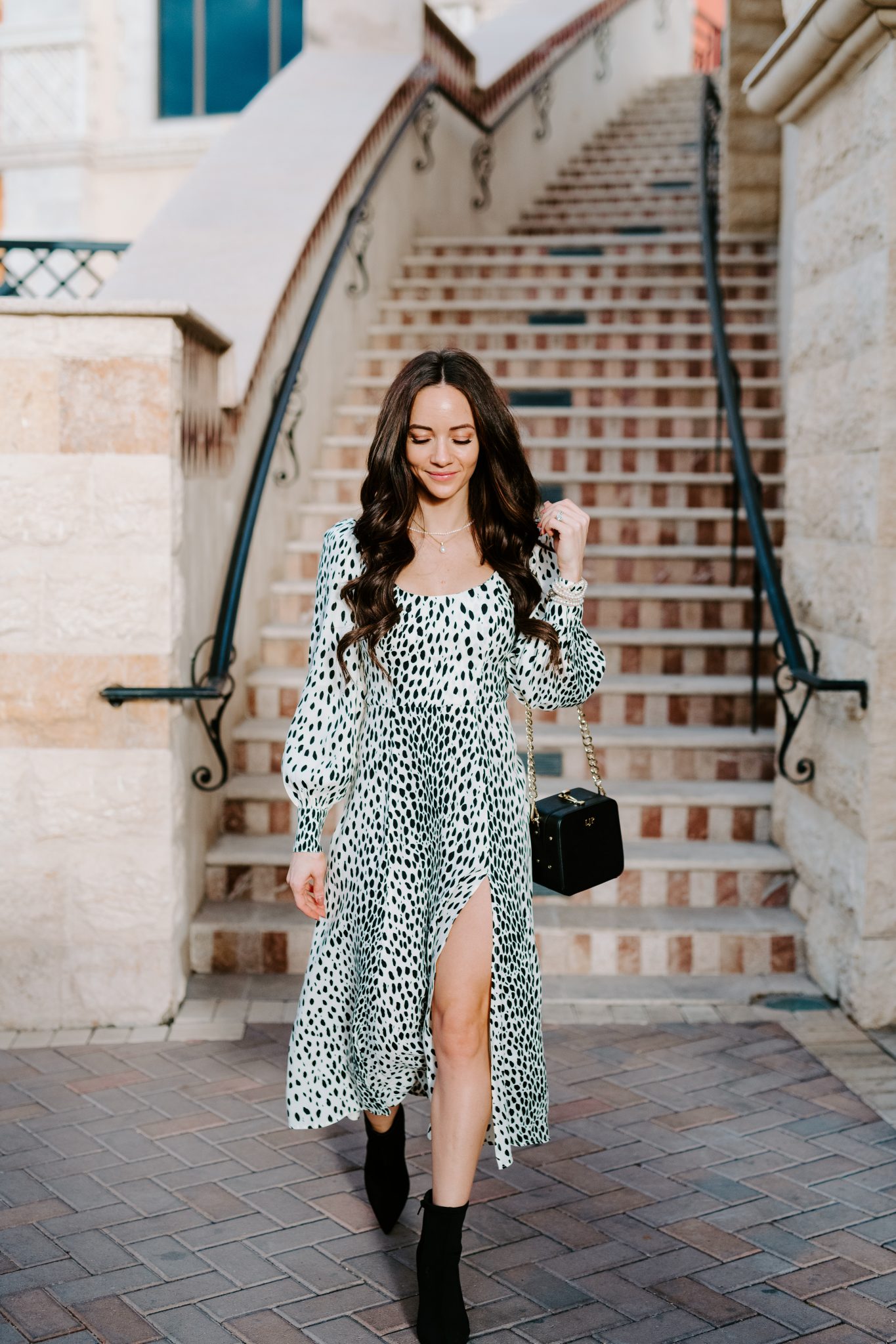Wedding Guest Dresses by popular Las Vegas fashion blog, Outfits and Outings: image of a woman wearing a long sleeve black and white print maxi dress with a high leg slit, pearl jewelry and carrying a square shaped black bag.