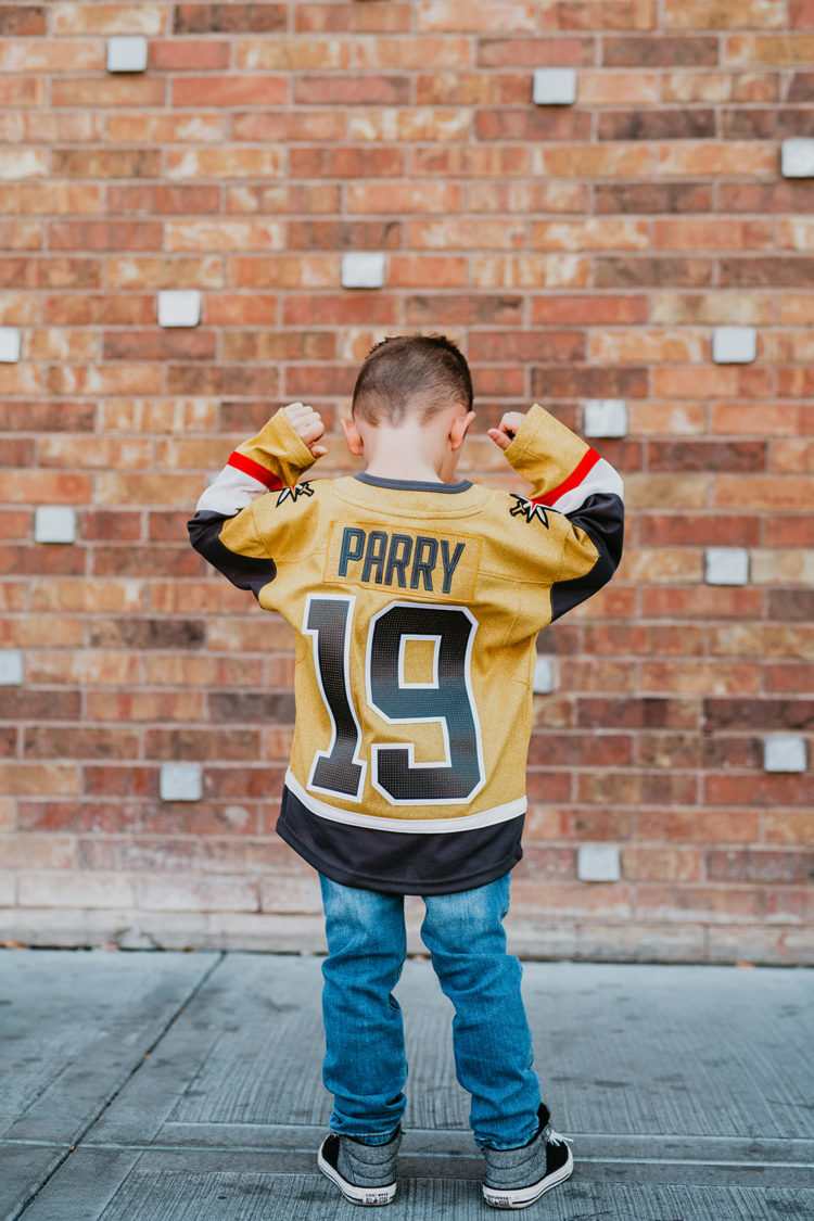 Golden Knights Gear by popular Las Vegas fashion blog, Outfits and Outings: image of a young boy standing in front of a brick wall and wearing a Golden Knights jersey. 