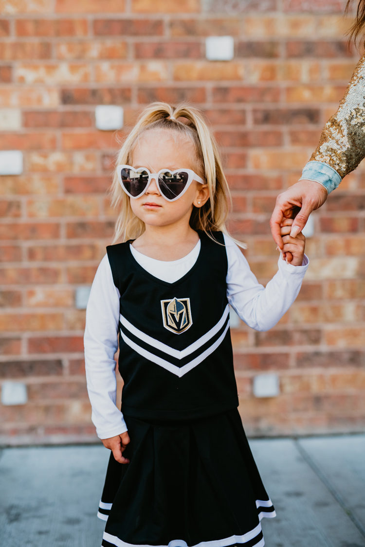 Golden Knights Gear by popular Las Vegas fashion blog, Outfits and Outings: image of a little girl wearing heart frame sunglasses and a black Golden Knights cheerleading uniform. 