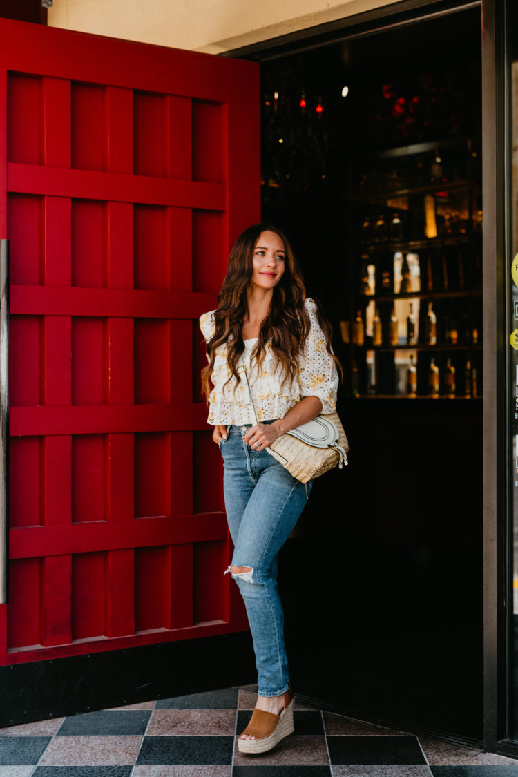 Eyelet Dresses by popular Las Vegas fashion blog, Outfits and Outings: image of a woman walking out of the doorway of a restaurant with a red door and wearing a white and yellow eyelet top distressed and a pair of espadrilles. 