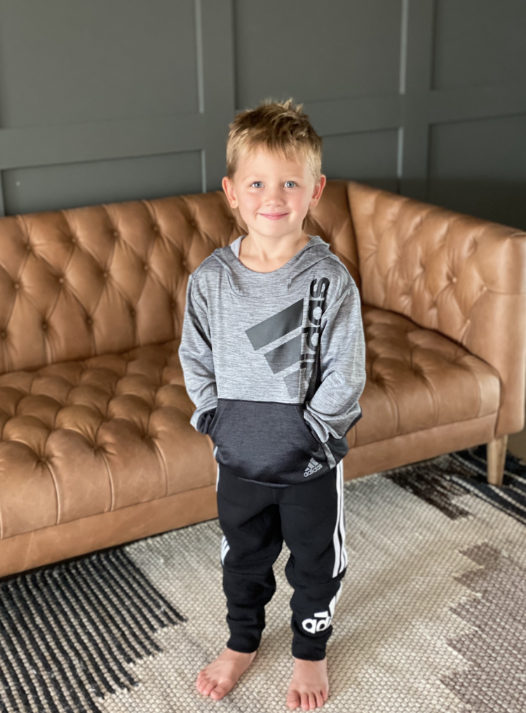 Nordstrom Anniversary Sale by popular Las Vegas fashion blog, Outfits and Outings: image of a little boy standing next to a brown leather Chesterfield couch and wearing an Adidas hoodie and Adidas black and white track pants. 