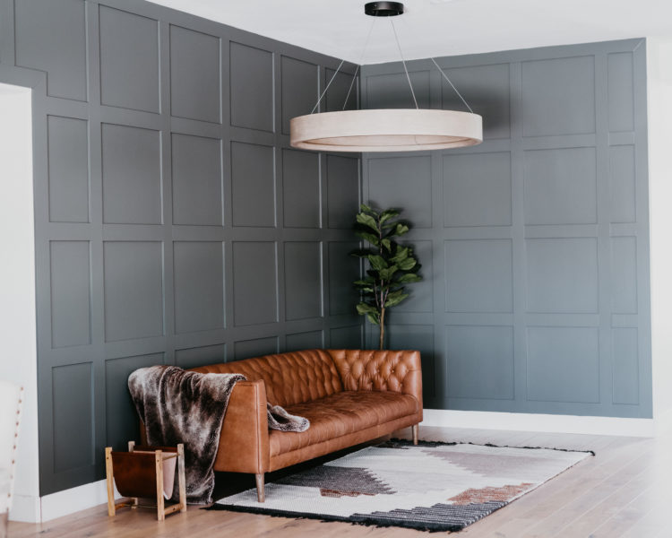 DIY Accent Wall by popular Las Vegas life and style blog, Outfits and Outings: image of a room with a grey board and batten wall, neutral color geometric area rug, brown leather Chesterfield couch, modern lighting fixture, and indoor house plant. 